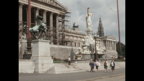 1950s: View of town in valley with green mountains in the background. Exterior of Austrian Parliament building with scaffolding and Pallas-Athena fountain in Vienna. Exterior Opera House.
