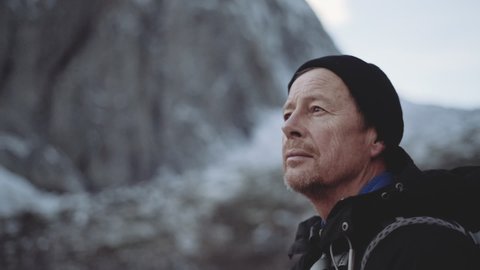 Medium Arc Handheld Slow Motion Shot Of Mature Hiker In Woolly Hat Looking Over Landscape, Norway