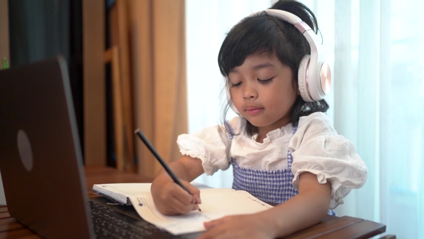 Asian kid girl school pupil wearing headphones studying online from home watching web class lesson or listening tutor by video call | Shutterstock HD Video #1063845511
