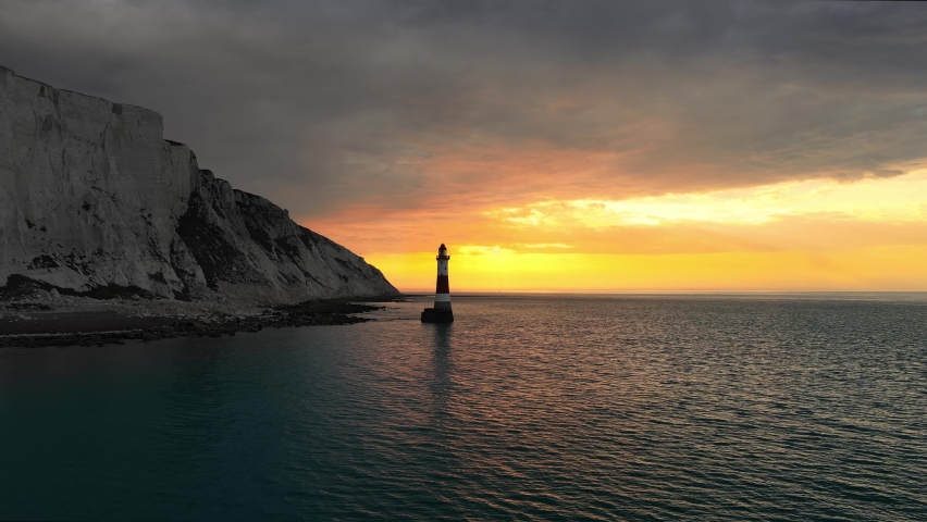 Landscape aerial drone footage video of a Beachy Head Lighthouse and chalk cliffs at colourful sunrise  with low tide in England, near Eastbourne Royalty-Free Stock Footage #1063847743