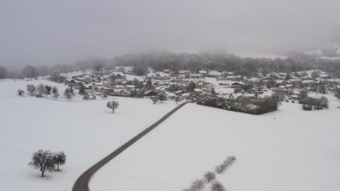 Andilly, Haute-Savoie french village under the snow, in the clouds and the mist. Drone aerial view during winter above the road