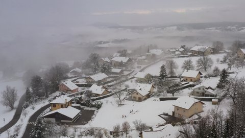 Andilly, Haute-Savoie french village under the snow, in the clouds and the mist. Saint Symphorien church and Vuache mountain in the bacground. Drone aerial view during winter