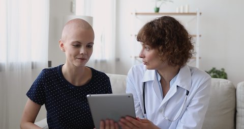 Focused 40s professional oncologist holding digital tablet, explaining treatment strategy to interested young woman with cancer disease, asking about health condition, showing chemo test results.