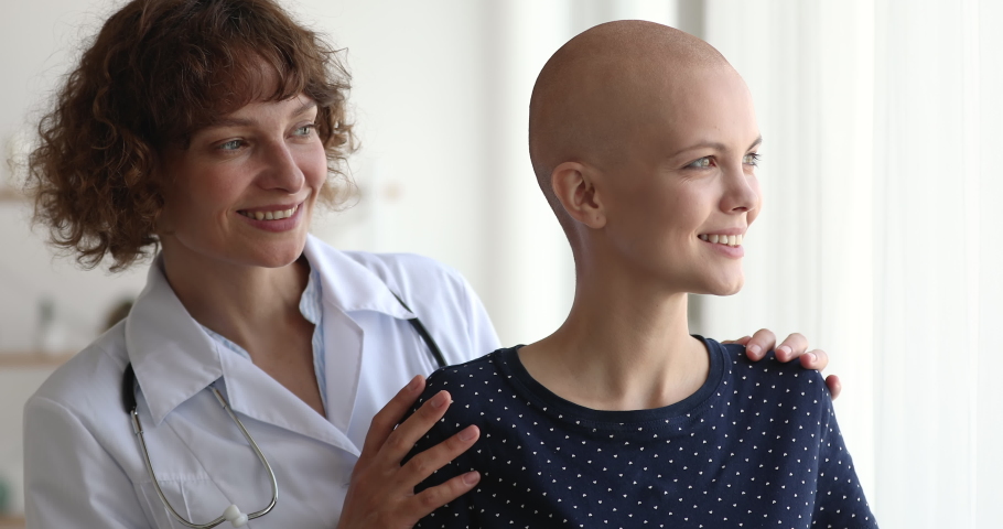 Smiling empathic 40s professional oncologist doctor in white uniform embracing shoulders of happy optimistic millennial female bald hairless patient, dreaming of full recovery, looking at camera. Royalty-Free Stock Footage #1063857421