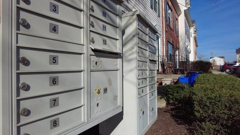 A woman is placing a letter she wishes to send in the outgoing box inside the metal cluster mailbox in her condo community. The outgoing mails are regularly taken up by postman who delivers mail.