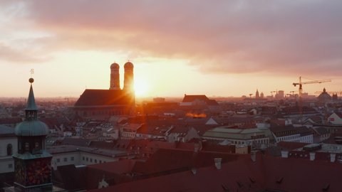 Famous German Cathedral Frauenkirche at Sunset Golden Hour light, located in City Center of Munich in Bavaria, Aerial dolly slide left with sun revealing behind Church Tower