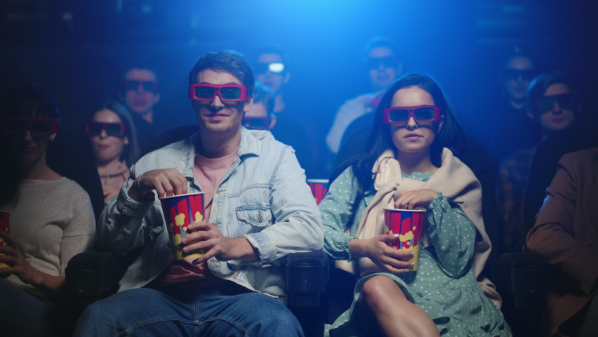 Cheerful friends having fun in cinema. Joyful couple laughing in movie theater. Happy woman and boyfriend eating popcorn in dark hall. Relaxed people spending weekend in cinema. | Shutterstock HD Video #1063863823