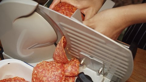 Chef slices salami on meat slicer machine. Outdoor event catering.