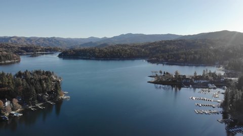 Aerial view over the calm, reflecting surface of lake arrowhead overlooking mountains, sunny autumn day, in California, USA - dolly drone shot