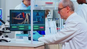 Elderly doctor writing on pc datas from test tubes in modern equipped laboratory. Multiethnic team of doctors examining vaccine evolution using high tech researching diagnosis against covid19 virus - Powered by Shutterstock - Get 15% off with code: PIKWIZARD15