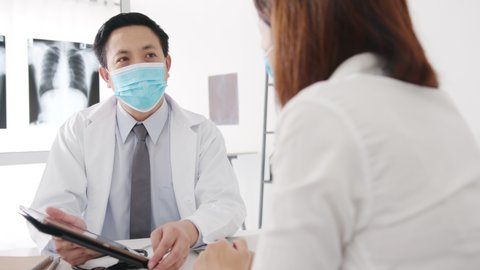 Serious Asia male doctor wear protective mask using tablet is delivering great news talk discuss results or symptoms with female patient in hospital office. Lifestyle new normal after corona virus.