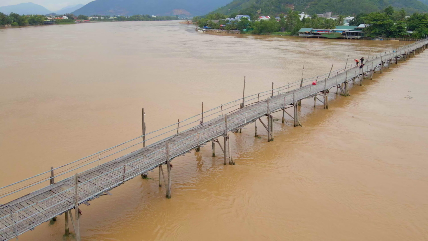 Aerial slowmotion shot of a wooden bridge across the river in Asia with motorbikes riding on it. Dangerous transportation constructions concept