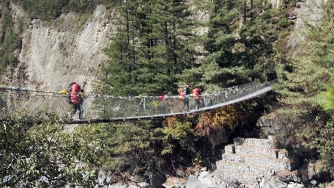 Sherpas and hikers walk a bridge crossing a valley. 
