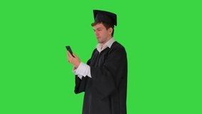 Smiling male student in graduation gown showing campus via video call on his phone on a Green Screen, Chroma Key.