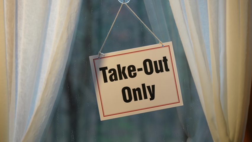Take Out Only sign swinging in the window of store front display in business concept. Camera pushes in.