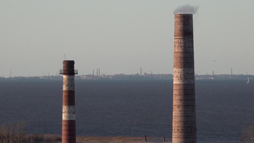 Factory with red pipes on the sea shore of the lake bay. There is smoke or steam. Kronstadt island on background. Close up view