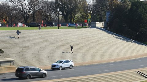 Washington, D.C. - United States - November 28 2020: A male jogger runs up and down the Watergate Steps in Washington, D.C. on a sunny autumn day. Cars, pedestrians and bicycle riders pass by.