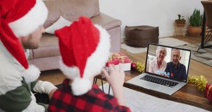 Caucasian man with son wearing santa hats on laptop video chat during christmas at home. communication with friends and family at christmas during covid 19 pandemic.