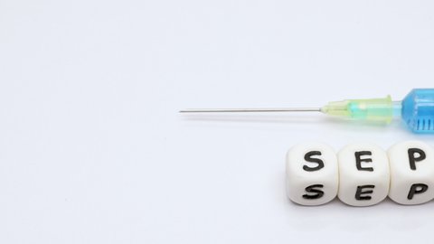 Slow panning on word sepsis spelt with white plastic cubes with a drug vial and syringe on white background. Sepsis awareness concept.