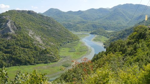 Blue river flowing through green valley toward distant mountains. Bends and curves of Crnojevica river in national park of Montenegro, meandering through the marsh among hills on way to lake Skadar.