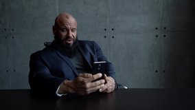 bald bearded businessman is communicating by smartphone by online video chat, sitting in office room