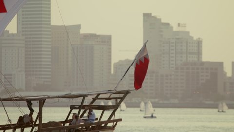 Manama, Bahrain - October 2018: Traditional Arabic Dhow with Bahrain flag branded sail during the sunset time in front of Manama Skyline