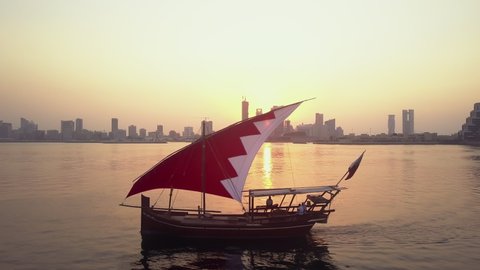 Manama, Bahrain - October 2018: Drone view of the Traditional Arabic Dhow with Bahrain flag branded sail during the sunset time in front of Manama Skyline