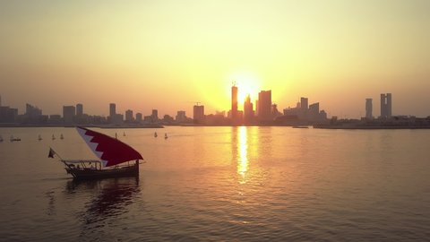 Manama, Bahrain - October 2018: Drone view of the Traditional Arabic Dhow with Bahrain flag branded sail during the sunset time in front of Manama Skyline
