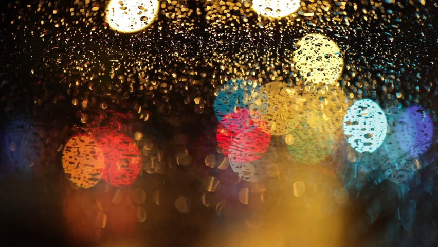 Multicolored lights of the evening city and passing cars through a wet rainy window. Abstract shot of evening city traffic bokeh. Rainy depressive weather. New York, USA