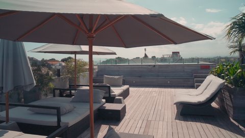 Pan of outdoor terrace overview in luxurious hotel with chaise-lounge and umbrellas