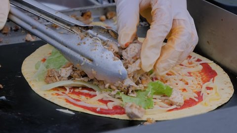 Slow motion: chef holding tongs and making mexican taco with meat at summer local food market - close up view. Outdoor cooking, gastronomy, cookery, street food concept