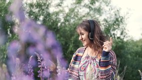 Pretty young happy woman in headphones dancing in a field of purple flowers