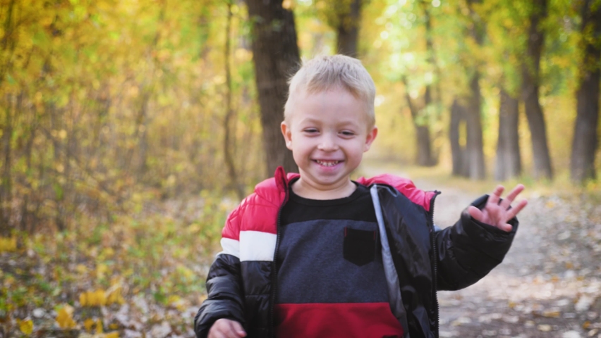Happy baby boy running in autumnal park. Little child playing on autumn walk. Autumnal forest with golden leaves. Steadicam video, 4K slow motion.