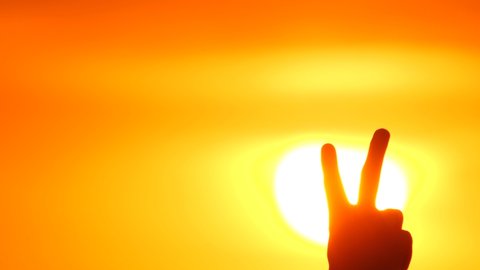 Peace Sign Hand. V-sign. Victory sign hand. Showing number two with fingers. Two fingers up in the peace or victory symbol. Orange Sky Background. Man's hand shows number 2. Gesture Victory or Peace