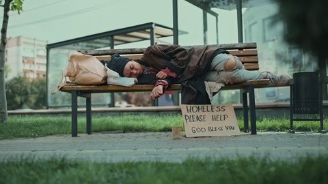 Homeless person sleeping on a park bench, indifferent people walking by