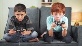 Two diverse kids seriously busy playing video game using joystick at home while sitting on sofa - concept of kids game concentration and leisure activity - Powered by Shutterstock - Get 15% off with code: PIKWIZARD15