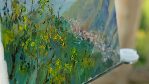 Close-up shot of landscape artist making final brush strokes with oil on canvas and finishing the painting en plein air