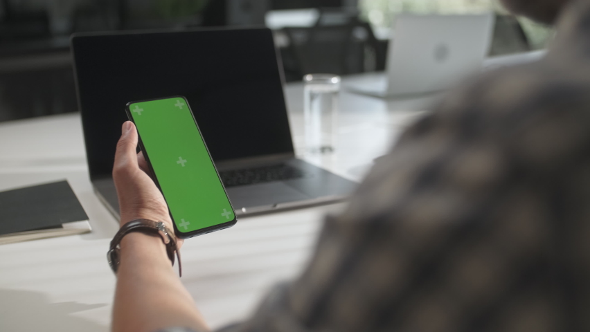 Over The Shoulder Shot Of a Business Man Working In Office Interior On Phone, Office Person Using Phone With Green Mock-up Screen Chroma Key Without Track Points Surfing Internet . Swipe Up Royalty-Free Stock Footage #1063934332