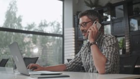 Focused Businessman Working on Laptop Computer in Office Interior. Male Worker Answering on Phone Call. Man Talking Smartphone at Remote Workplace. Business Man Calling Phone at Office - Powered by Shutterstock - Get 15% off with code: PIKWIZARD15