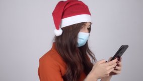 A young woman in a Santa Claus hat in a medical mask chatting on the phone and thinking. Celebration amid the coronavirus pandemic. High quality 4k footage
