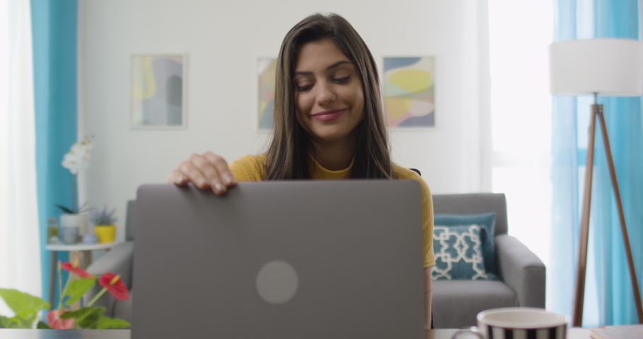Dolly out of confident and cheerful caucasian brunette woman opening and typing on a laptop. Young female professional writing an important email from her home. Modern living room. Remote working. Royalty-Free Stock Footage #1063936087