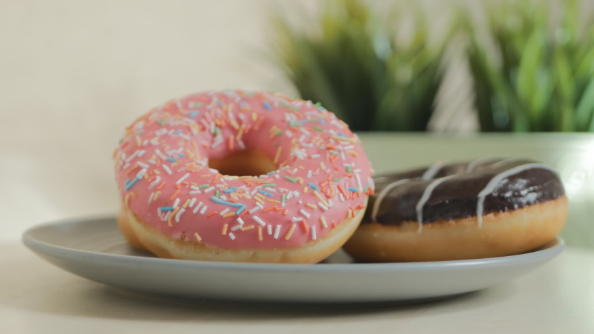 donuts with pink and chocolate icing in a plate rotate. Copy space. Close-up