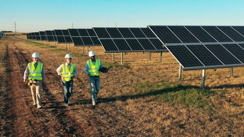 Three solar energy specialists walking at a solar power facility. Professional engineers discuss innovative project.