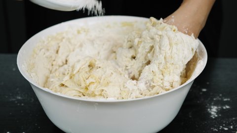 Baker is adding salt to yeast dough. Process of preparing pastry for pizza. Female hands mixing ingredients in bowl for cooking dough. Kneading dough. Making a delicious treat or dessert