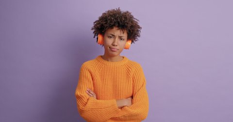 Frustrated dark skinned woman with curly hair does facepalm gesture says oh no I forgot regrets doing something wrong disappointed by her failure uses headphones poses against purple studio wall