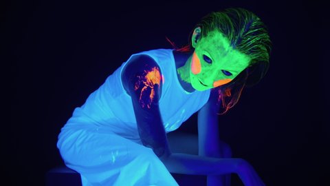 Shooting of sitting woman with scary painted face in ultraviolet light