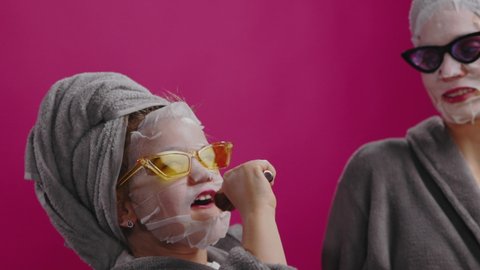 Cheerful mother and daughter in beauty masks sunglasses having fun together in bathroom during skincare routine. Funny little girl singing like superstar.
