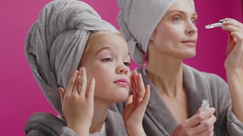 Young beautiful famlily of mother and daughter doing skincare in bathroom applying moisturizing serum product for fresh shiny skin. Feminine. Couple.