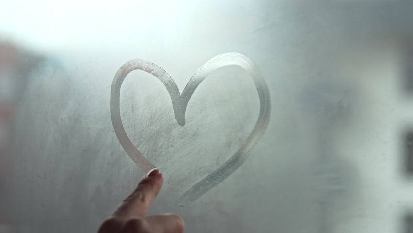 A hand draws a heart shape on the window with her finger. Fell in love. Shares love with the whole world and charity concept. Selective focus. Royalty-Free Stock Footage #1063950472