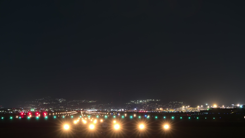 Time lapse shot of airport runway at night hour. Planes quickly arrive and departure. Bright edge and approaching lights on ground, dark sky. Motion blur silhouettes of airliners Royalty-Free Stock Footage #1063950916